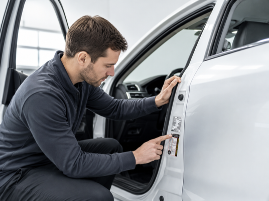 Person checking a vehicle paint code label inside a car door shut